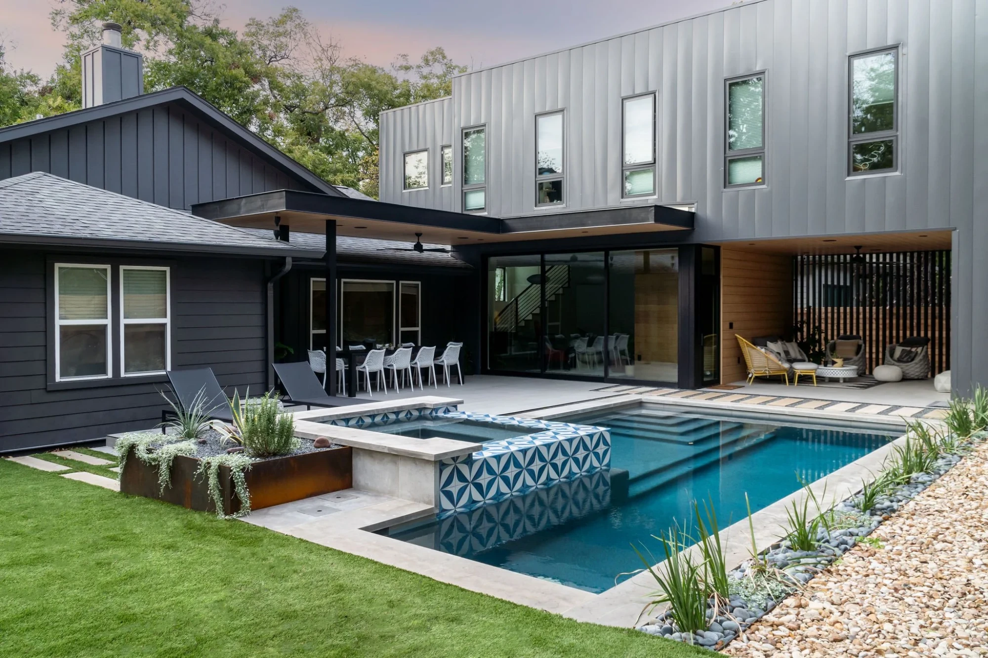 Geometric pool with blue-tile raised spa and steps up to a black modern home and patio in Austin