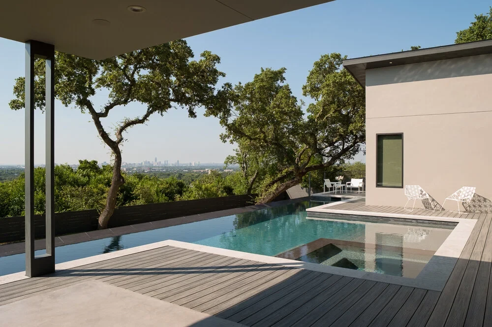 Infinity pool and spa on a hillside terrace overlooking the Austin skyline, framed by oaks off a covered patio