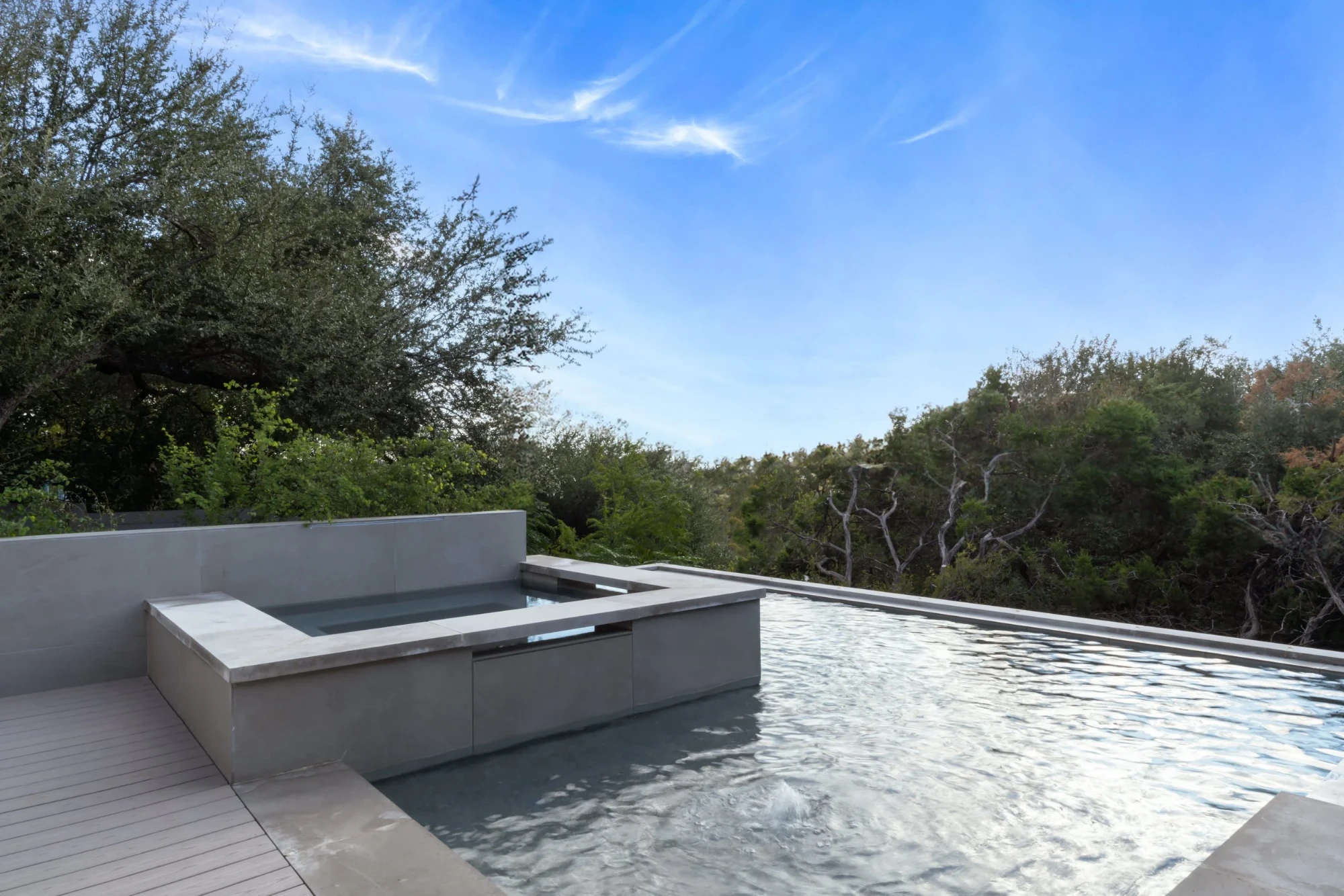 Concrete infinity pool and raised spa overlooking green treetops and Hill Country in Rollingwood