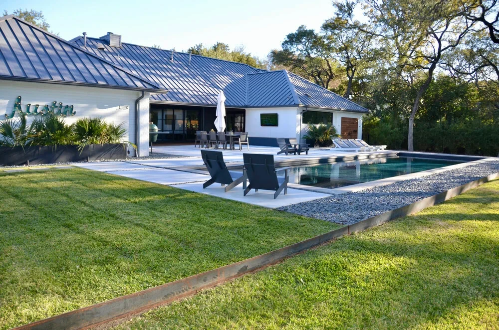 Geometric pool beside a metal-roof home on a wide lawn in West Lake Hills at golden hour
