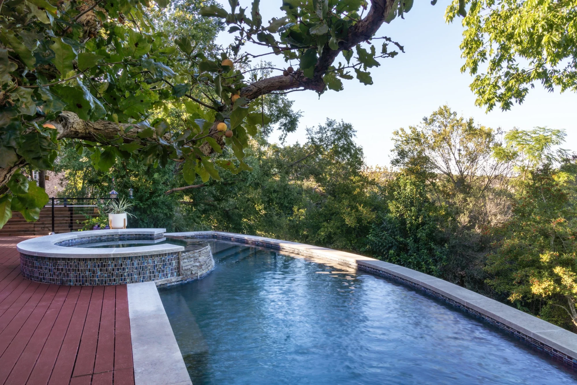 Infinity pool and round stone-clad spa overlooking the Hill Country, with mosaic tile, ipe deck and an oak overhead