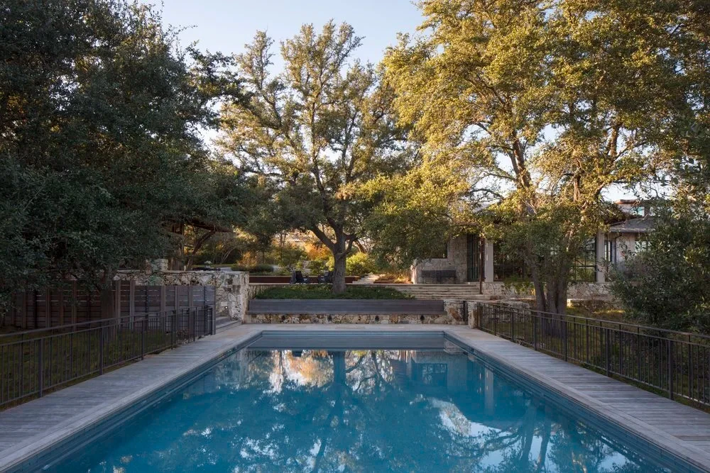 Geometric pool ringed by stone coping under live oaks at golden hour in the Hill Country