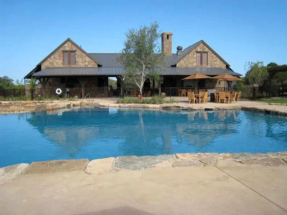 Large freeform pool with stone deck before a Hill Country stone lodge in Spanish Oaks