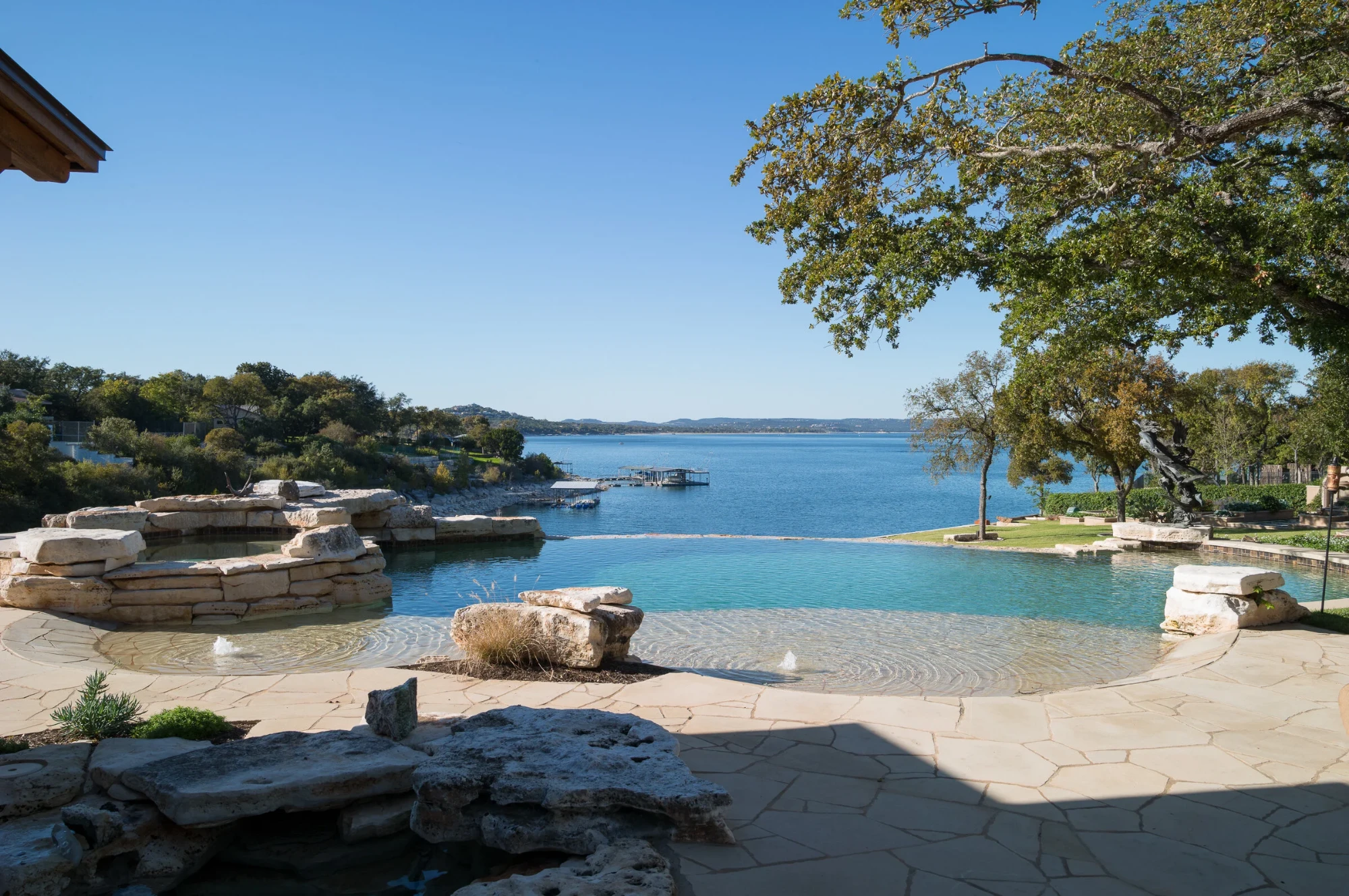 Infinity pool with a vanishing edge over Lake Travis, stacked-stone spa and flagstone deck under live oaks