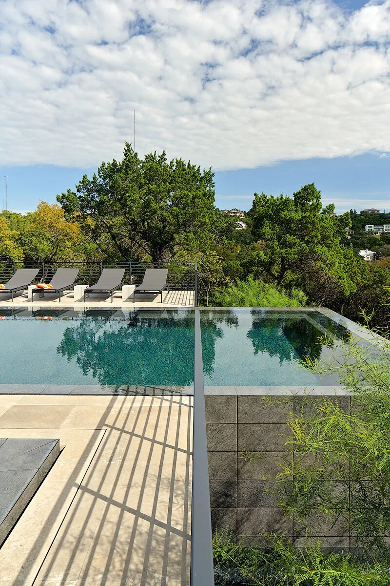 Geometric pool with an infinity edge and lounge chairs above a tree line in West Lake Hills
