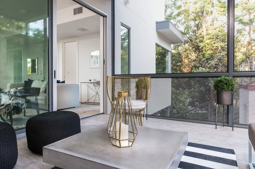 Covered patio with concrete-top table, looking through glass walls into a bright open kitchen