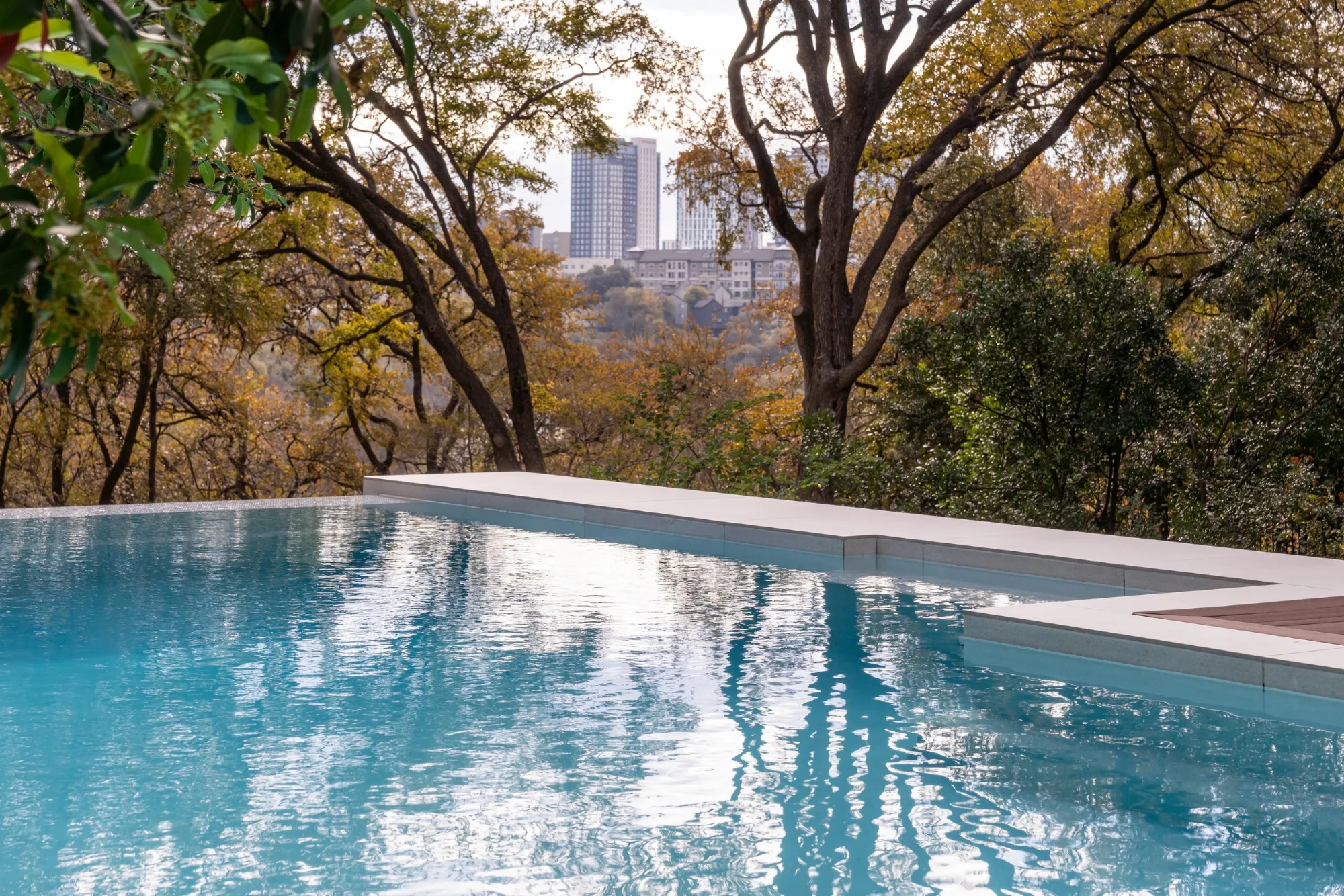 Infinity pool reflecting fall trees with the downtown Austin skyline visible through the canopy