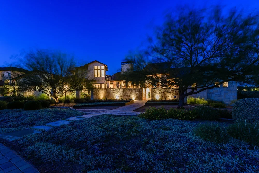 Stone Hill Country home glowing at twilight above native landscaping and a curved driveway