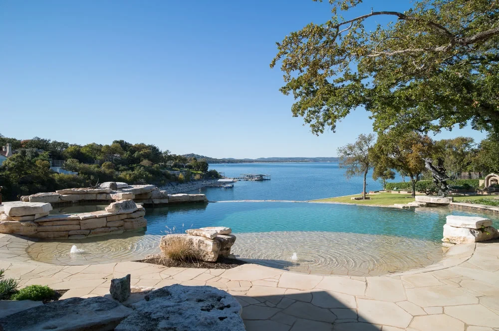 Freeform infinity pool overlooking Lake Travis, with a stone spa and natural flagstone deck