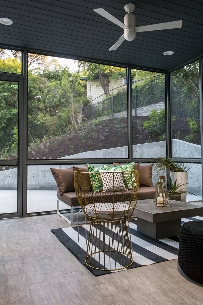 Screened porch with ceiling fan, leather sofa and striped rug, walls of glass to a hillside