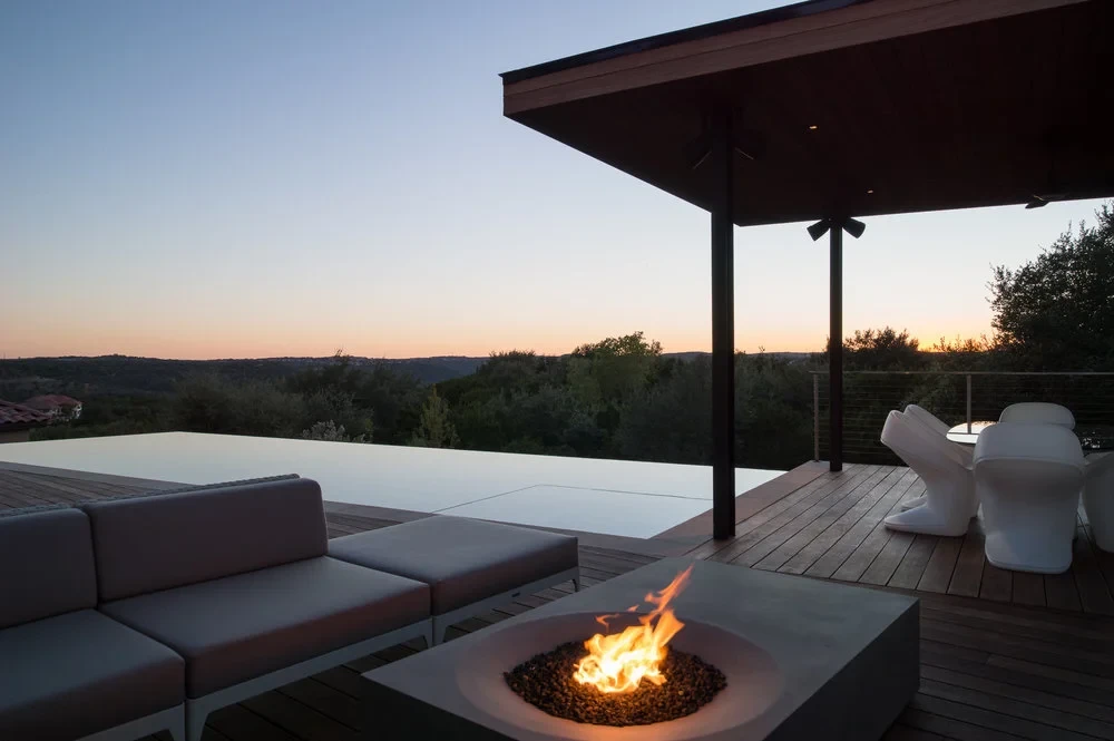 Covered deck with a concrete fire pit and lounge sofa overlooking the Hill Country at sunset