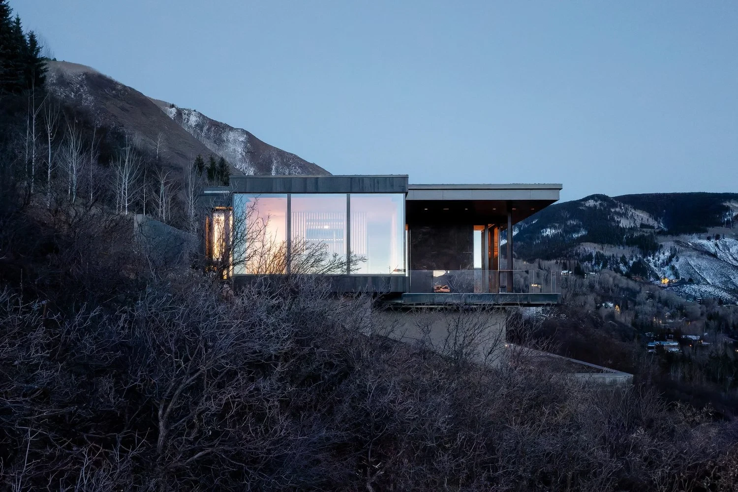Glass-walled modern home cantilevered over a snowy Aspen hillside at twilight