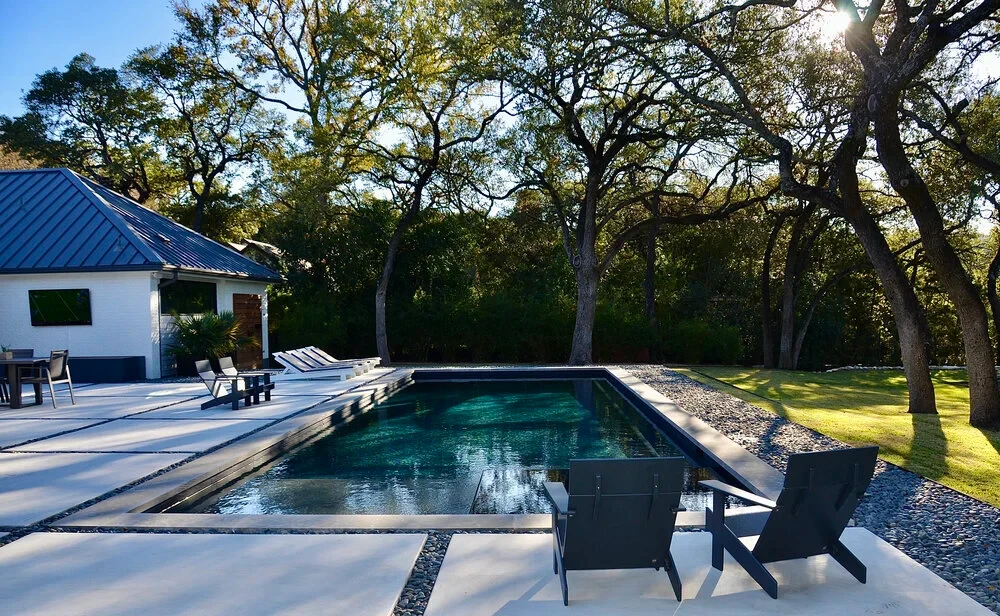 Geometric pool with lounge chairs beside a white home, framed by oaks in West Lake Hills