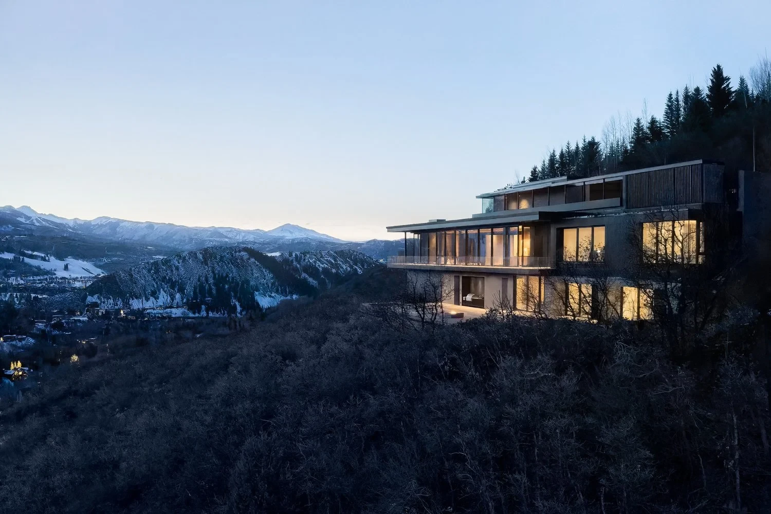 Lit modern home perched on a ridge above the snow-dusted Aspen valley at dusk