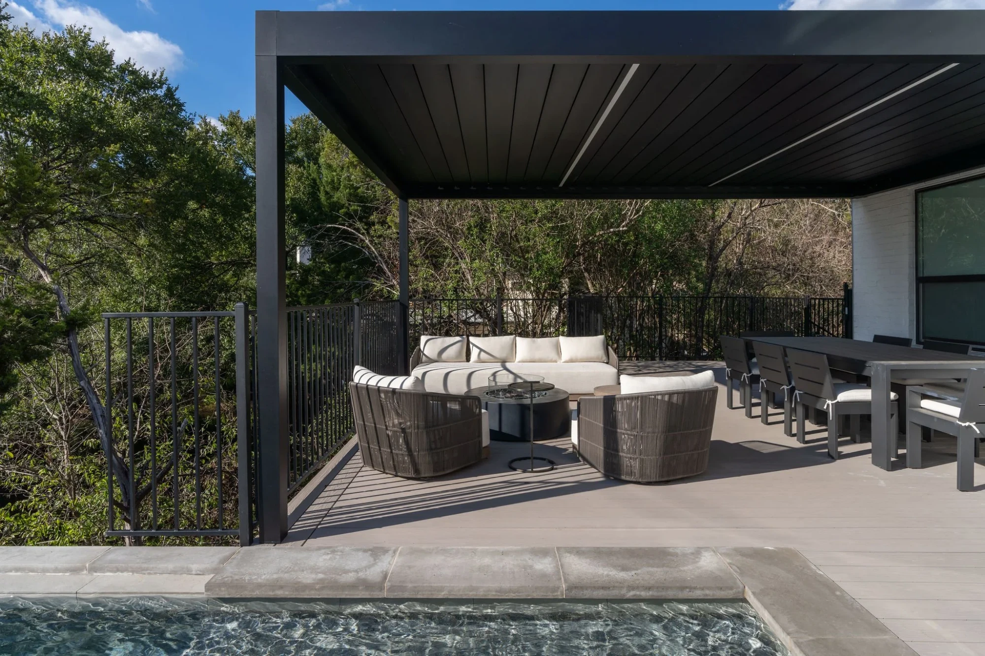 Deck with a black pergola and wicker seating beside an infinity pool over the Hill Country