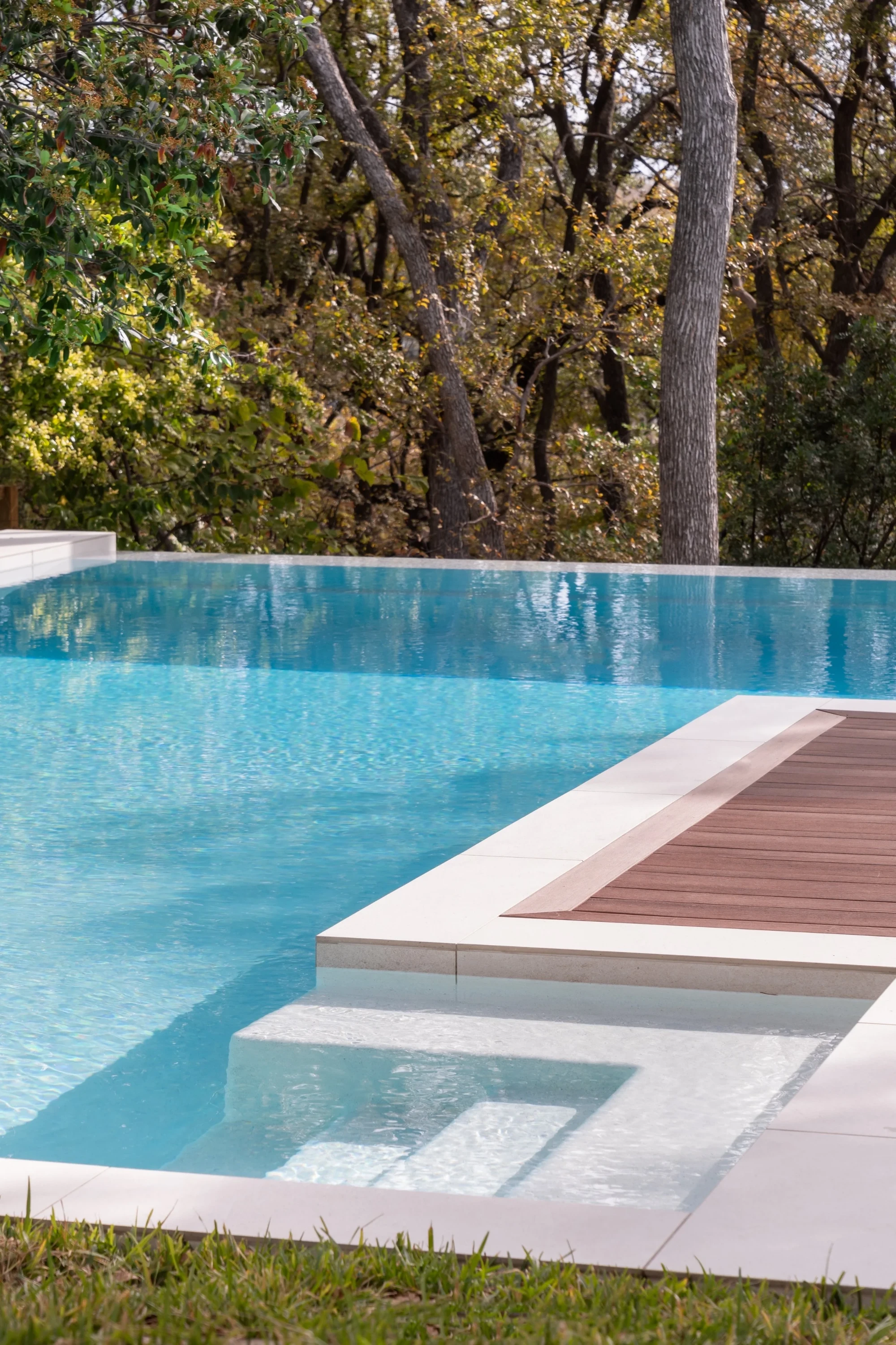 Infinity pool with stone coping and a wood deck inset, beside fall woods in West Austin