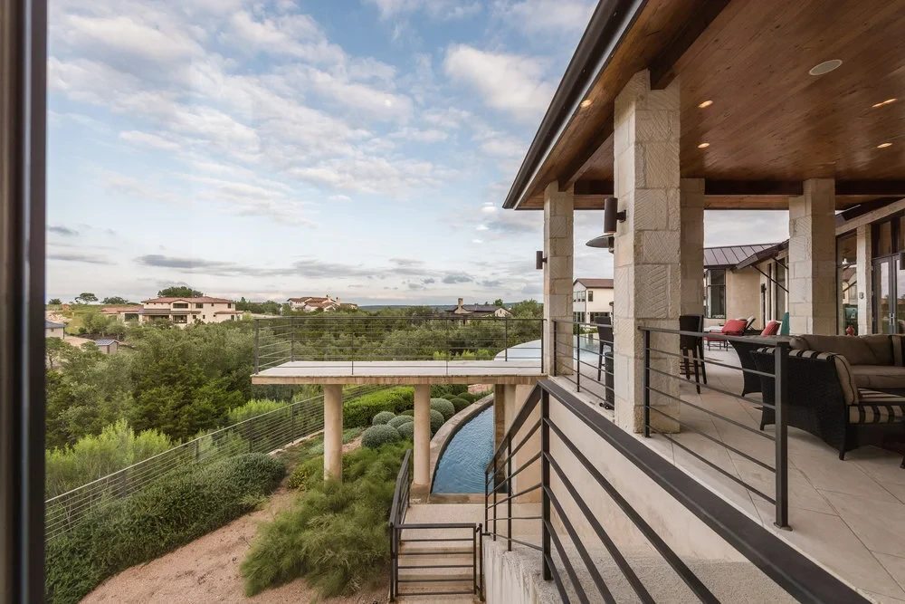View from a covered stone patio over a cantilevered infinity pool on columns above the Hill Country