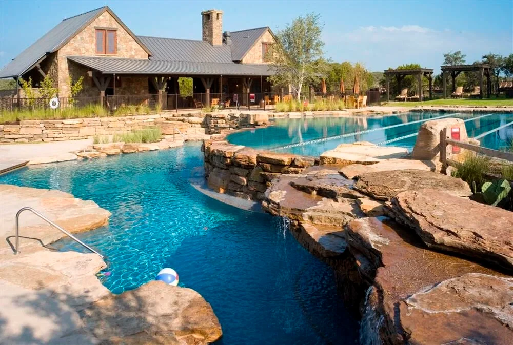 Freeform pool with stone waterfalls and boulders before a stone lodge in Spanish Oaks