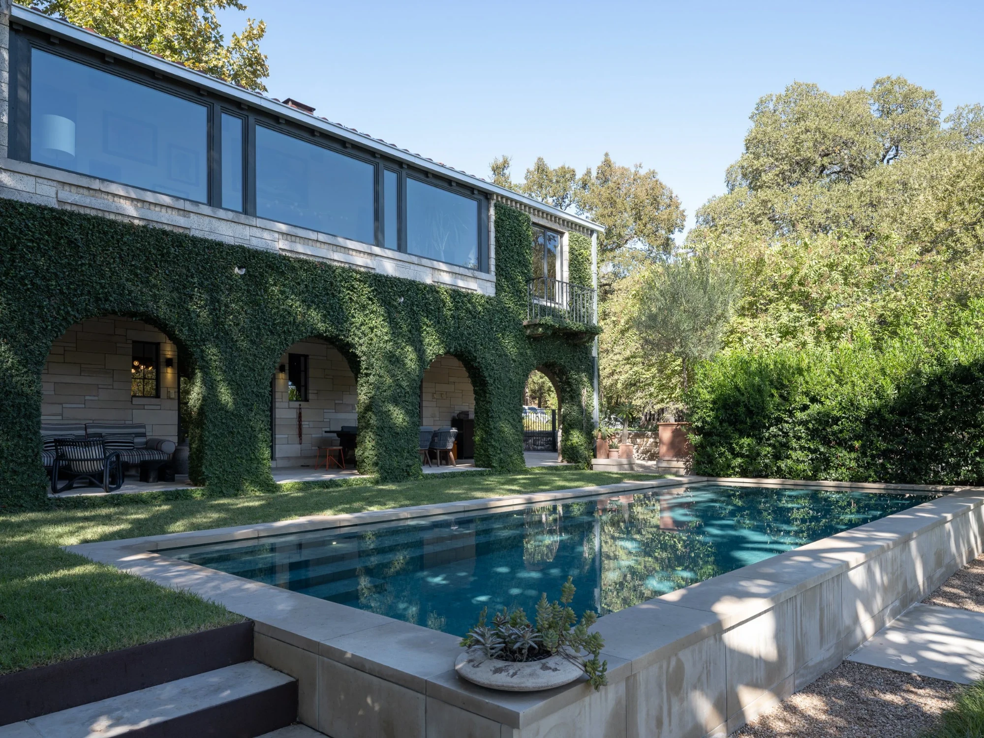 Geometric pool reflecting an arched ivy-covered home, with stone steps and a planter