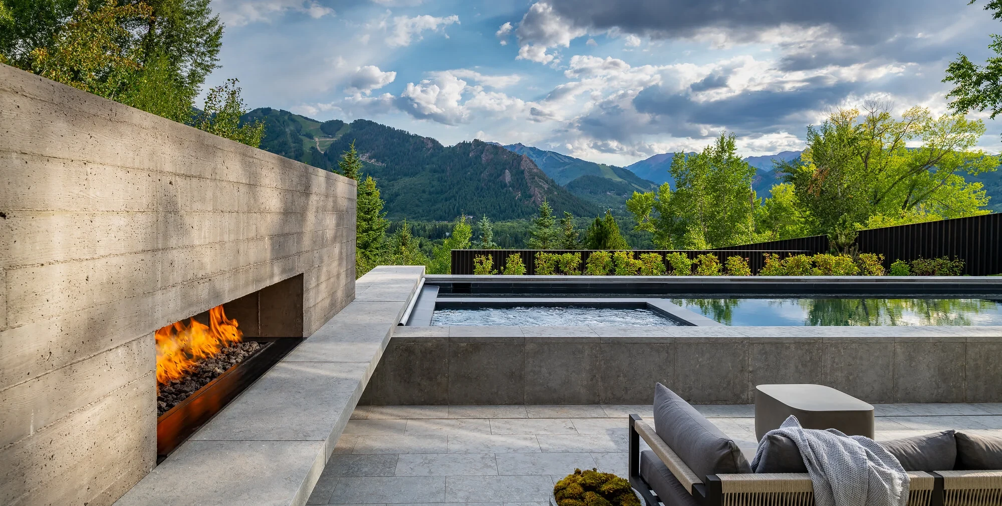 Geometric pool and concrete fireplace on a terrace overlooking the green Aspen mountains