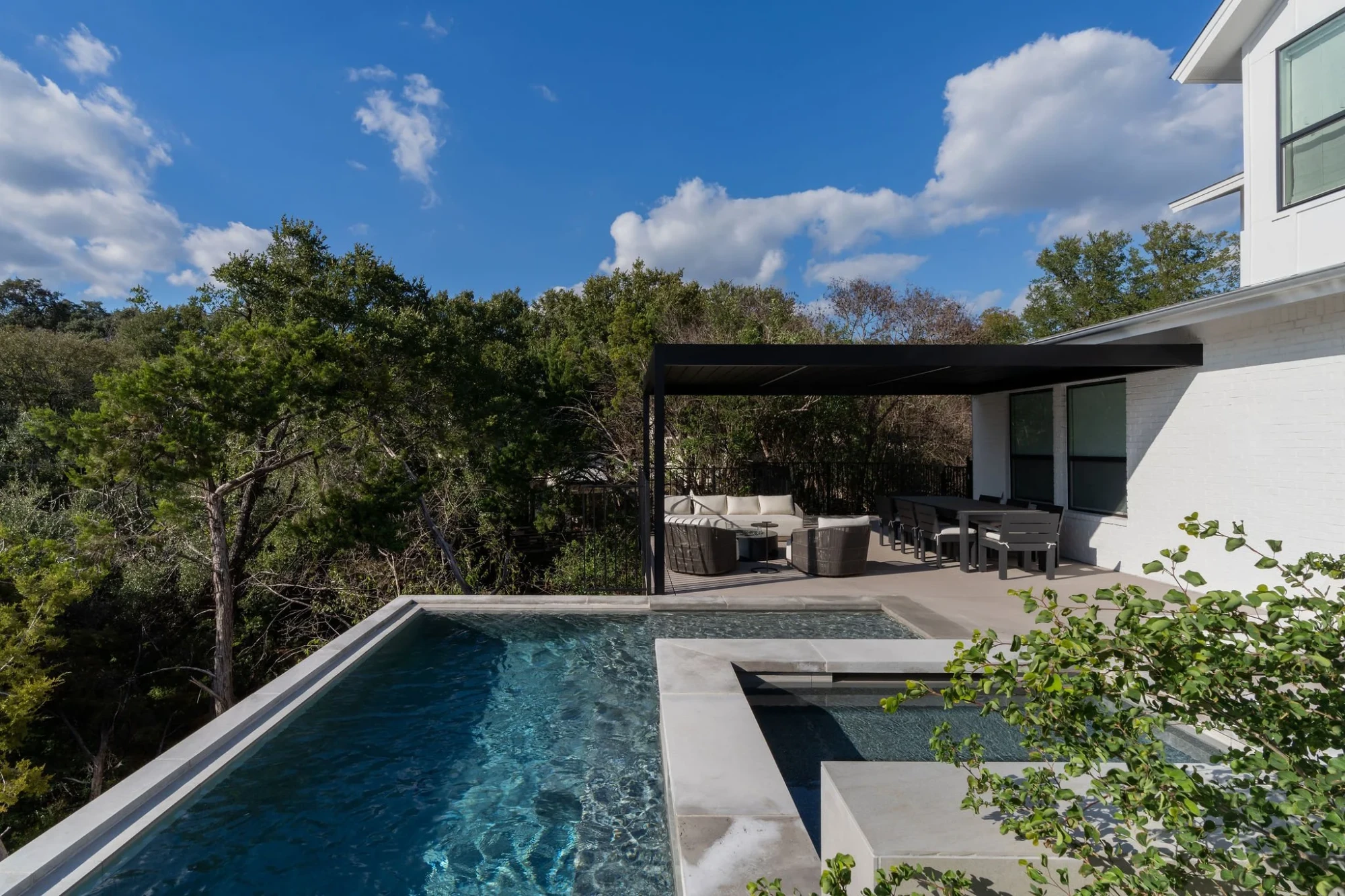 Infinity pool and raised spa with a black pergola and lounge over treetops in Rollingwood