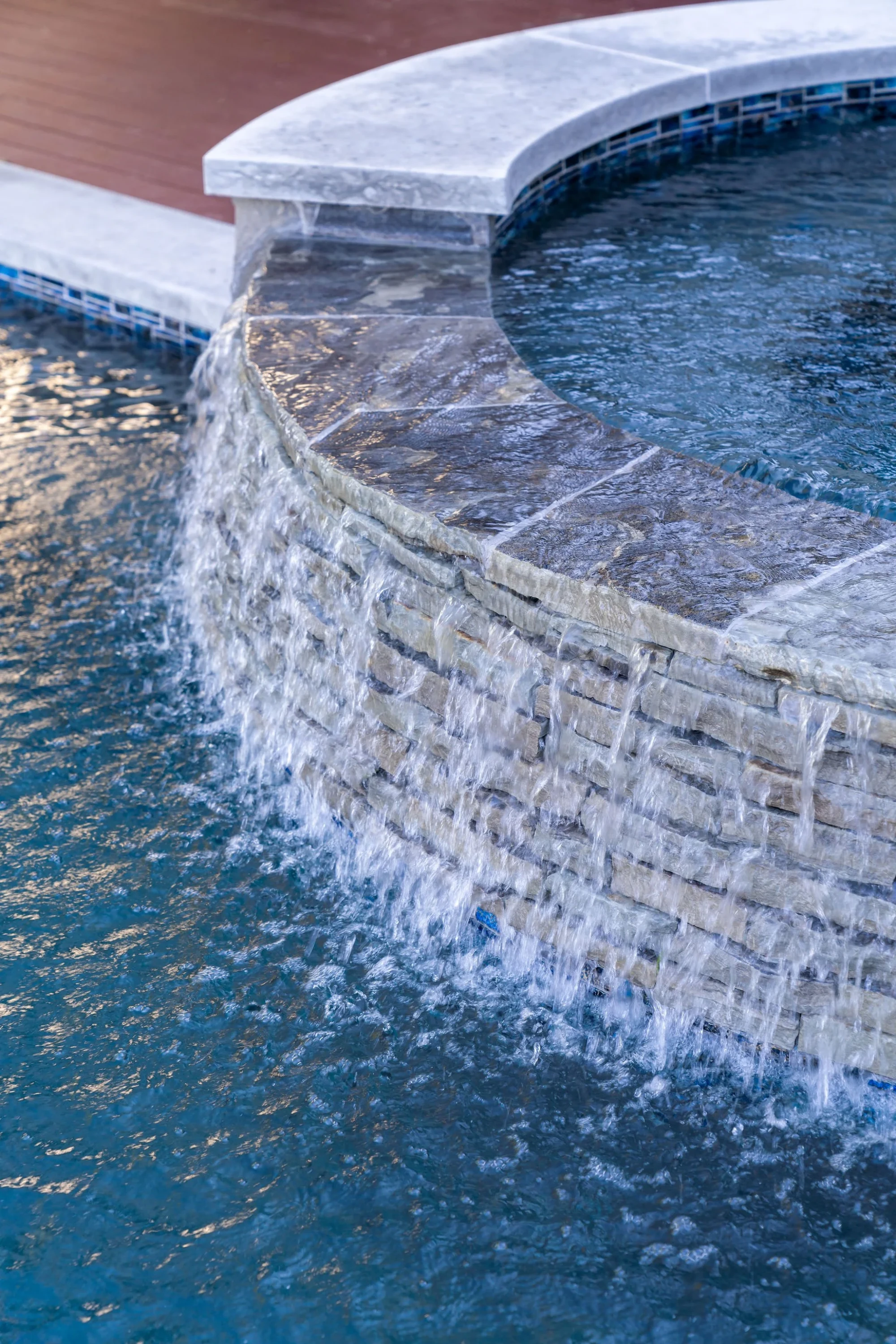 Travertine spa wall with a sheet waterfall cascading over stone into the pool below, close detail view