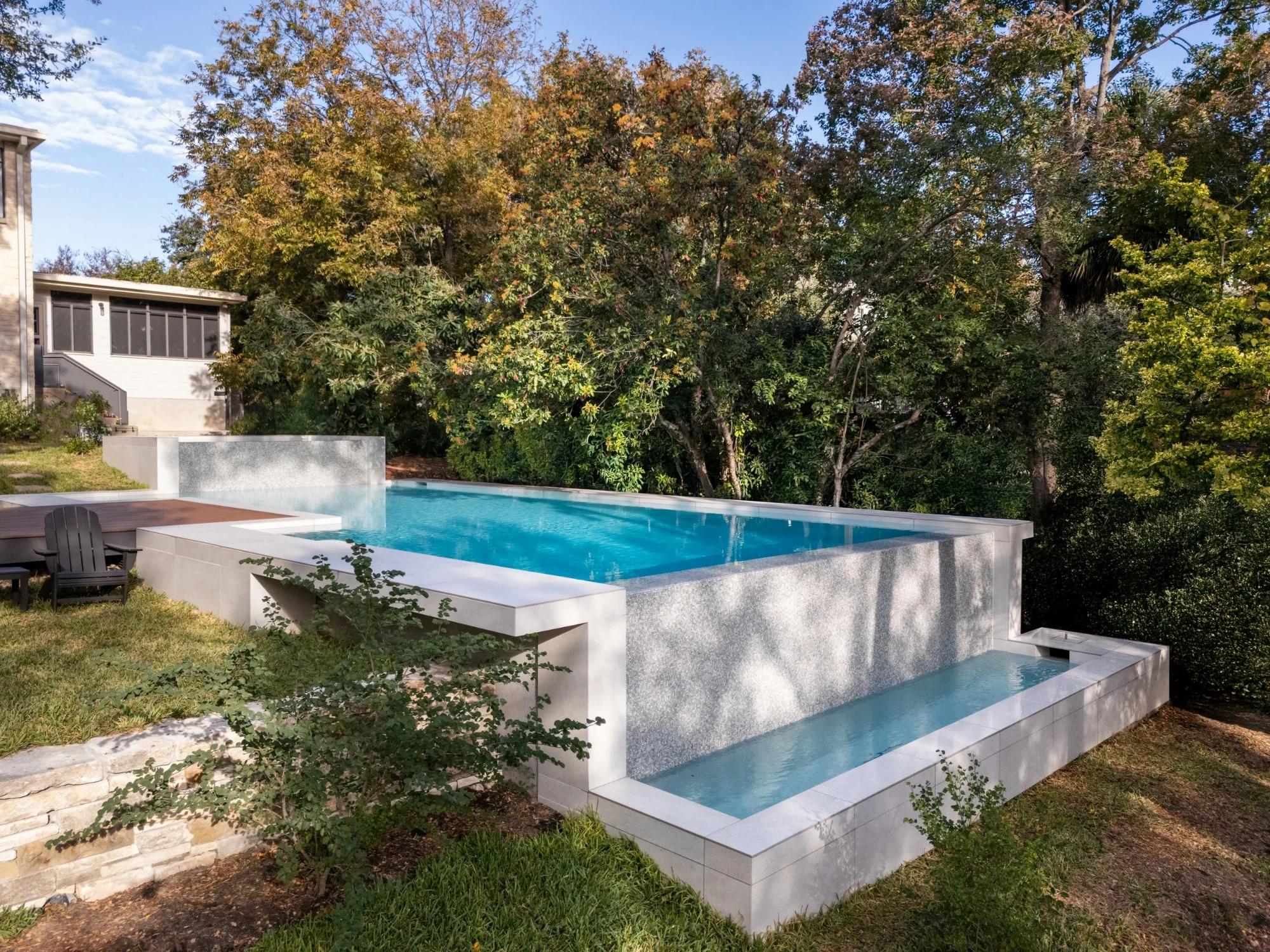 Raised infinity pool with a spa spillway and limestone walls in a wooded West Austin yard