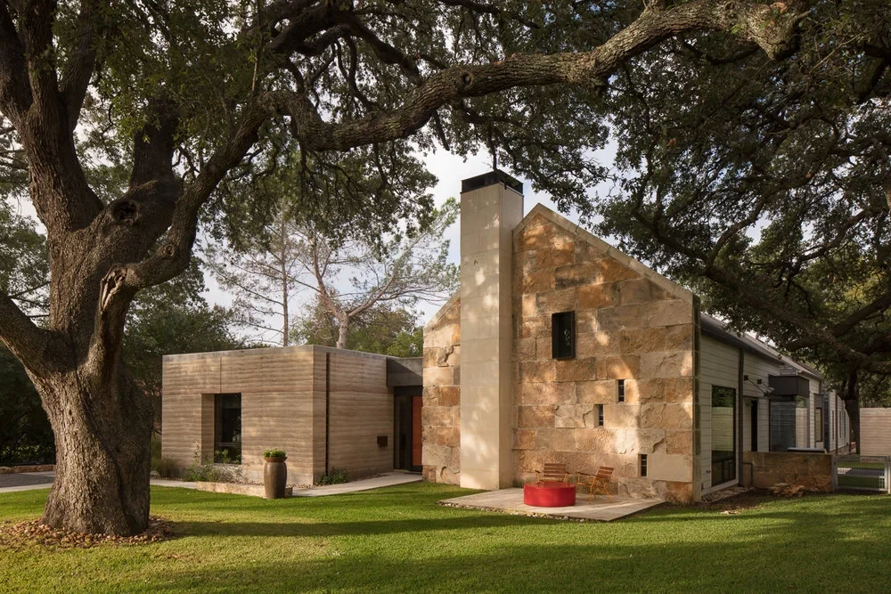Stone-walled Hill Country home with a tall chimney and metal roof, framed by a large live oak