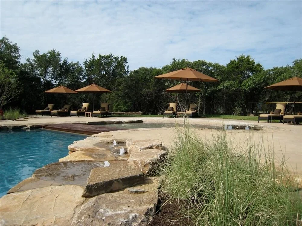 Freeform pool with a flagstone deck, umbrellas, and grasses by the trees in Spanish Oaks
