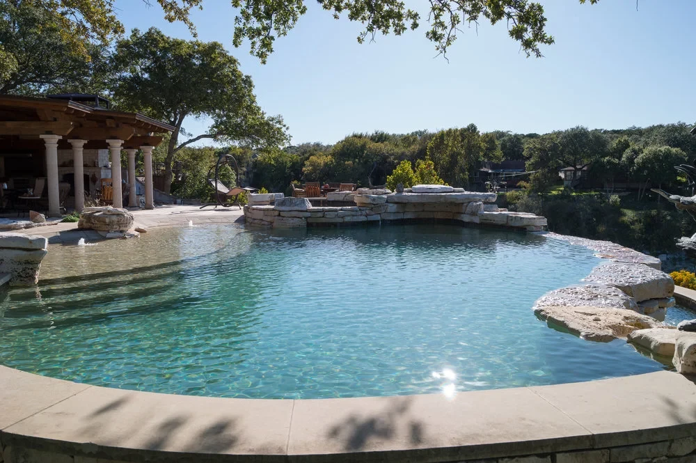 Freeform pool with stone coping and a covered patio, set among live oaks above Lake Travis