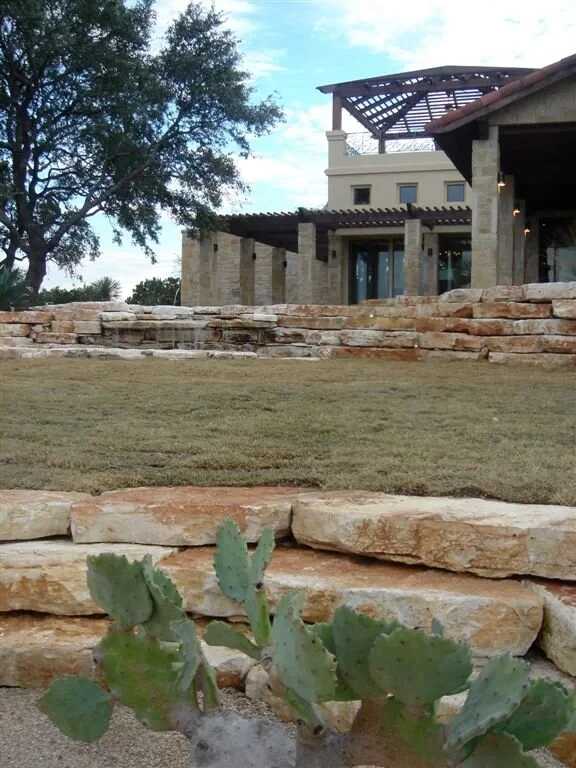Stone lodge with a pergola above tiered limestone walls, lawn and prickly pear in the foreground