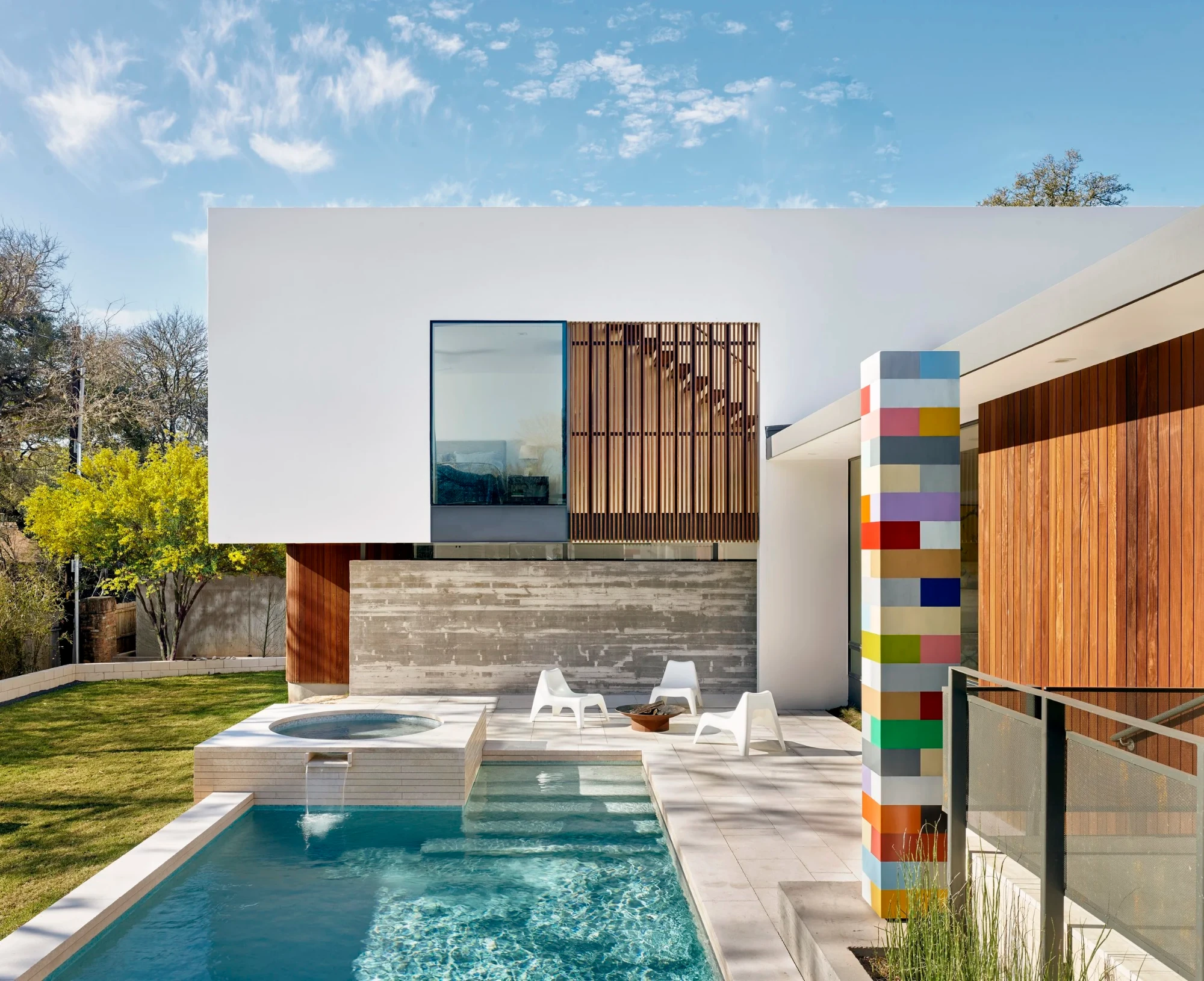 Geometric pool and raised spa with a spillway, white modern home, and colorful tile sculpture