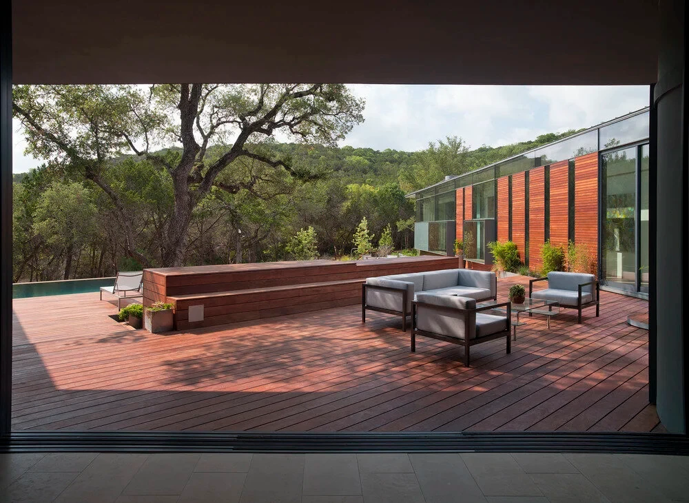 Wood deck with patio furniture viewed from inside, looking out to oaks and Hill Country slopes