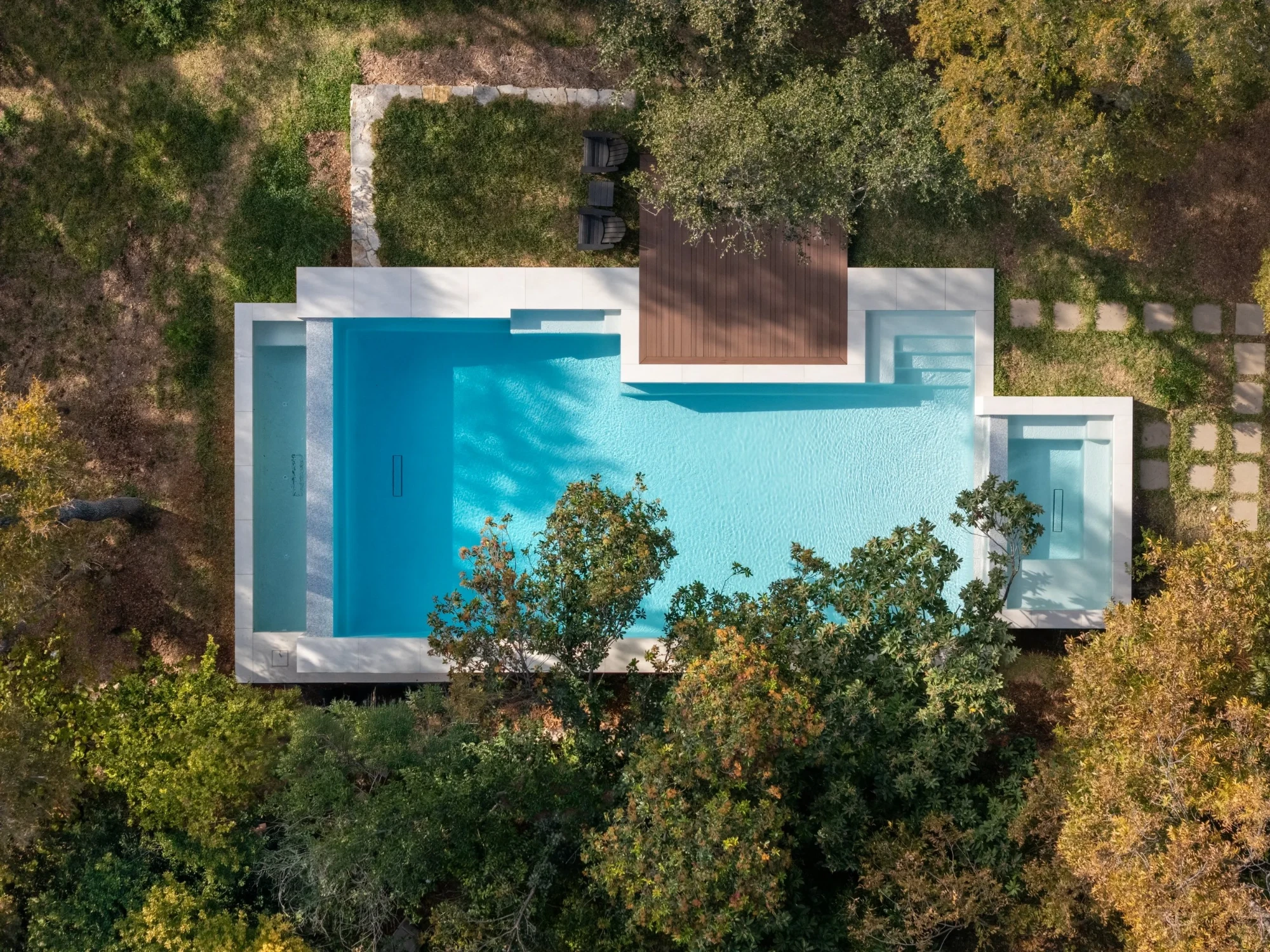 Overhead view of a raised geometric pool and spa with wood deck amid West Austin treetops