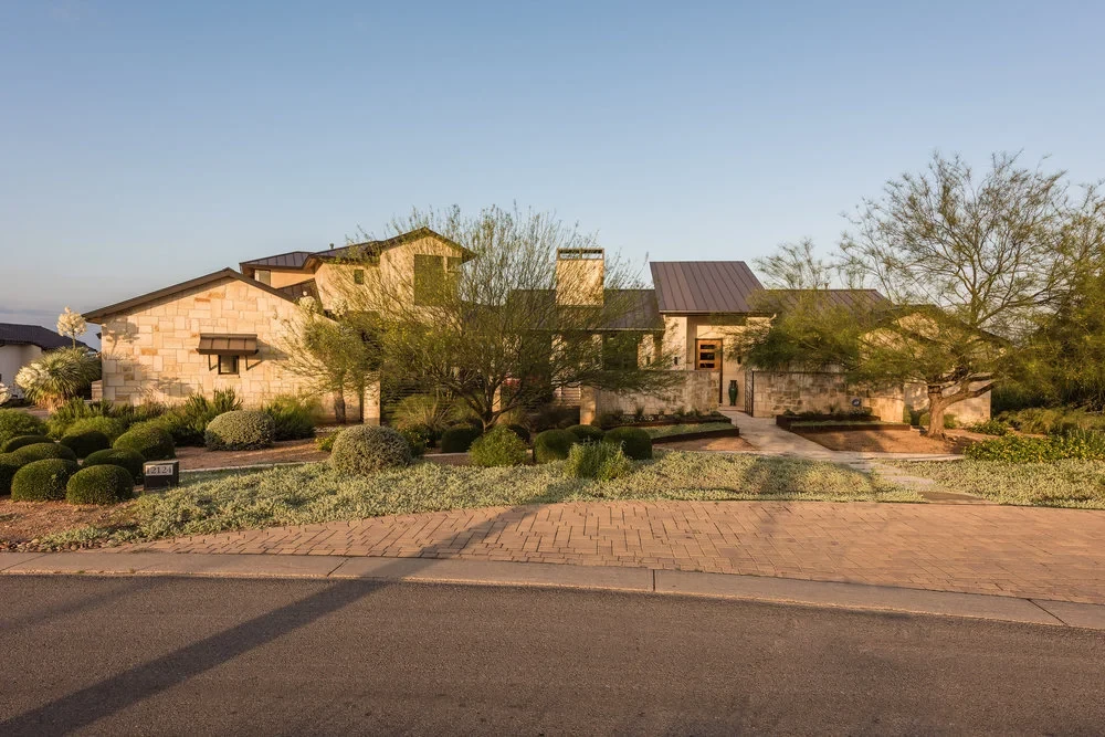 Stone Hill Country home at dawn set among native trees and landscaping along a quiet street