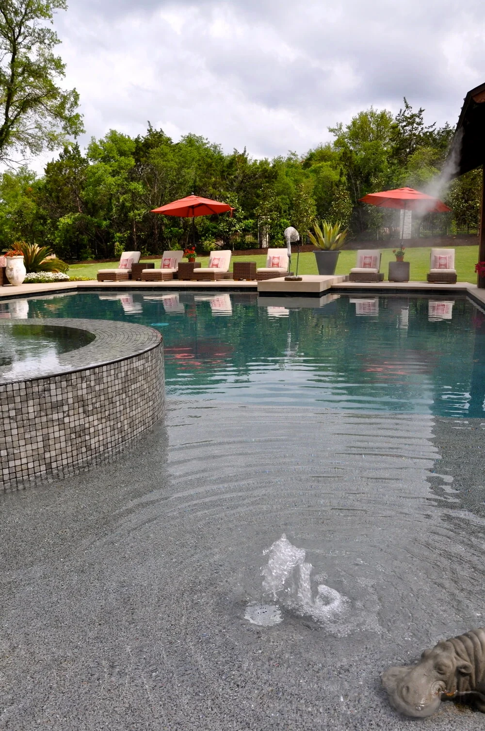 Geometric pool with mosaic-tile spa, bubbler, and red umbrellas over lounge chairs in West Lake Hills
