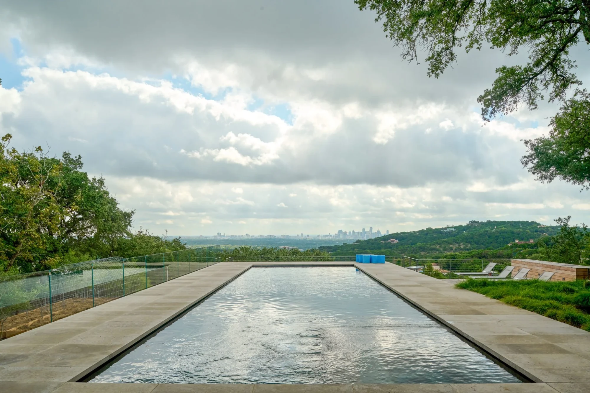 Infinity pool with a limestone deck under cloudy skies, the Austin skyline on the horizon beyond the edge