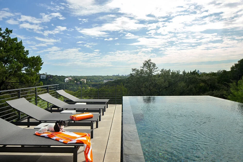 Infinity pool with lounge chairs overlooking the West Lake Hills under a cloudy sky