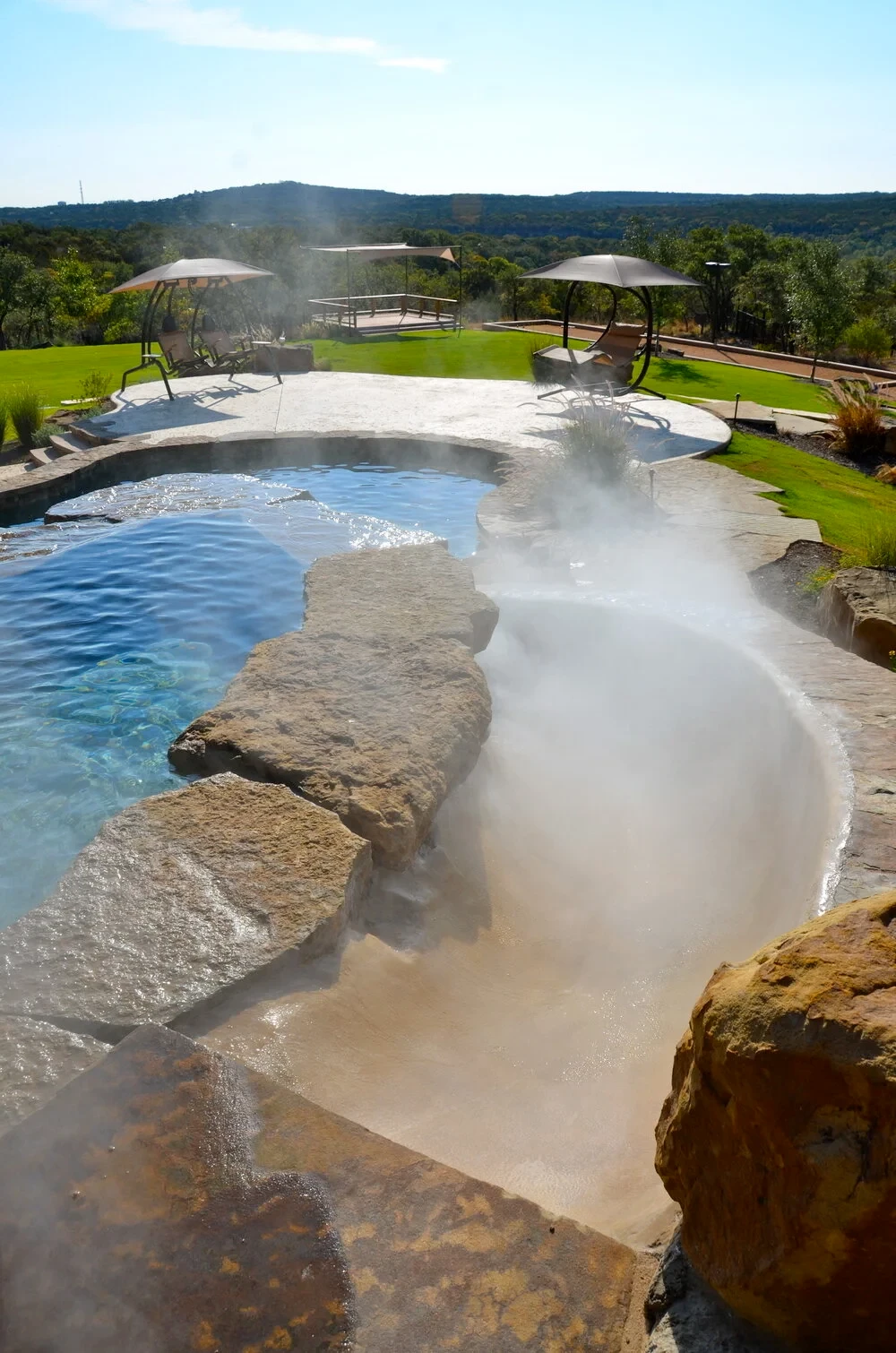 Freeform pool with a stone waterfall and canopy lounge chairs overlooking the rolling Hill Country