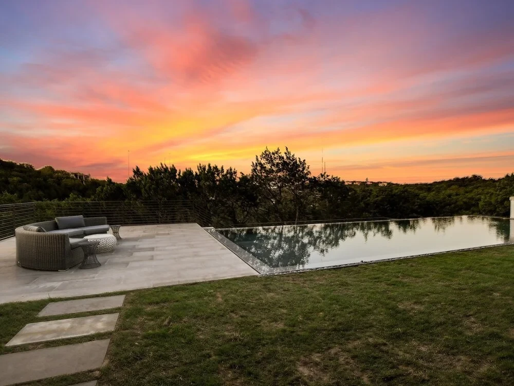 Modern home with an infinity pool and stone deck overlooking forested Hill Country hills