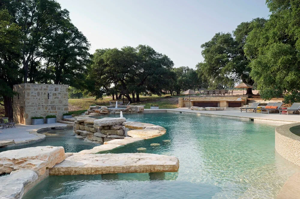 Freeform pool with stone spillways and ledges set in a wide lawn dotted with oaks