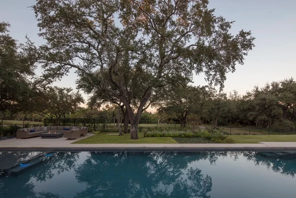 Geometric pool reflecting a broad oak and dusk sky, surrounded by lawn in Barton Creek