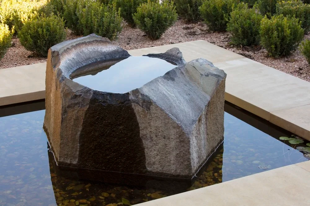 Carved stone fountain boulder spilling into a square reflecting pool edged by clipped boxwoods