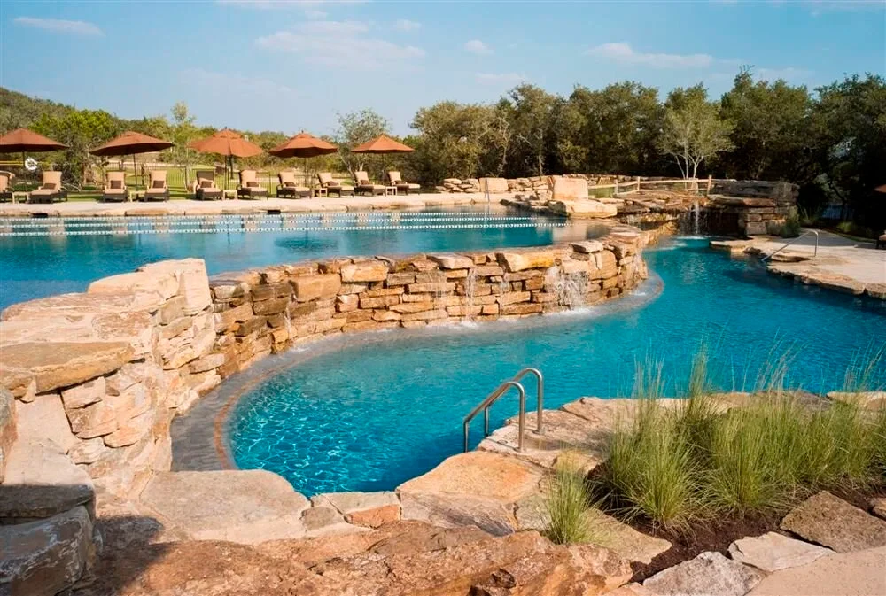 Freeform pool with stone waterfalls and boulders framed by trees in Spanish Oaks