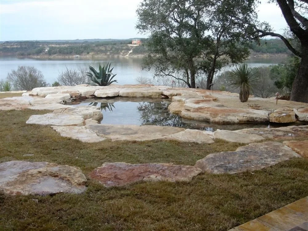 Natural stone spa edged in limestone overlooking a lake and wooded hills in the Hill Country