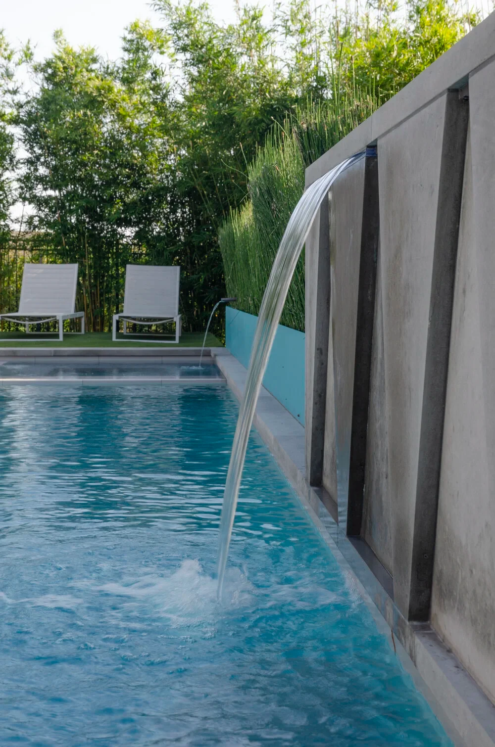 Sheer-descent water feature spilling into a geometric pool with loungers and bamboo behind
