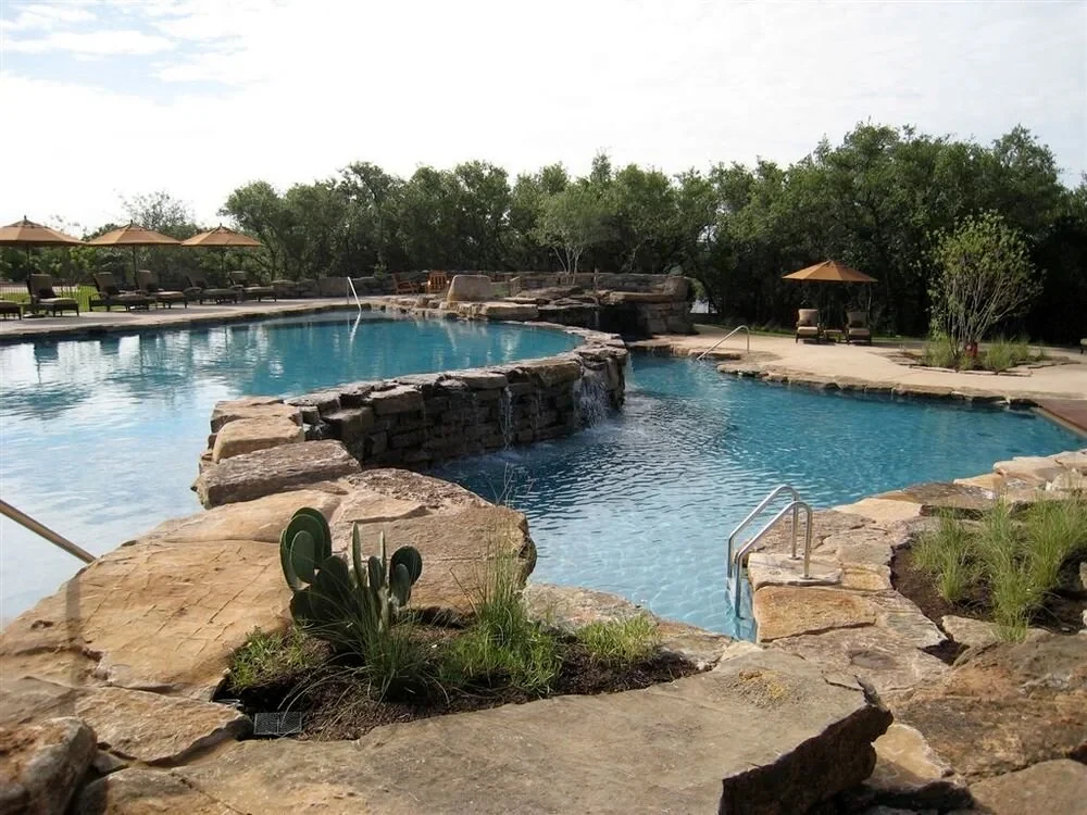 Freeform pool with stone islands, waterfalls, and a pavilion among trees in Spanish Oaks