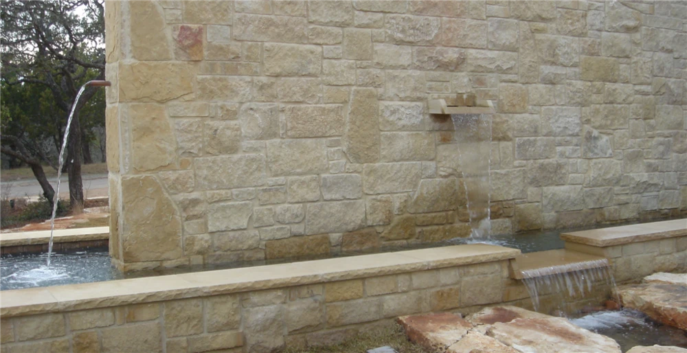 Stone wall with copper scuppers and a sheer waterfall spilling into a long limestone water trough