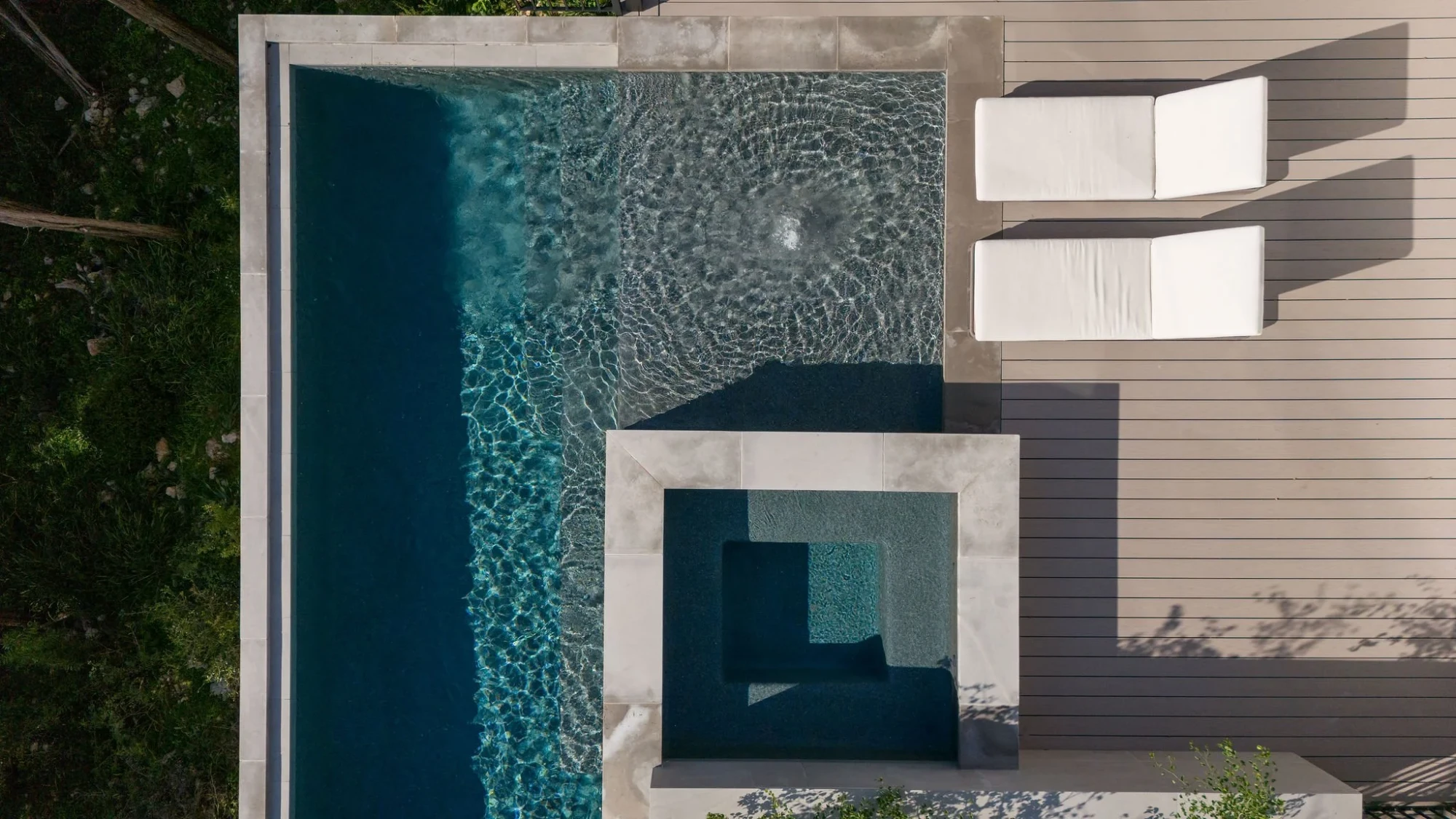 Aerial of an infinity pool with a square spa and white loungers on a wood deck in Rollingwood