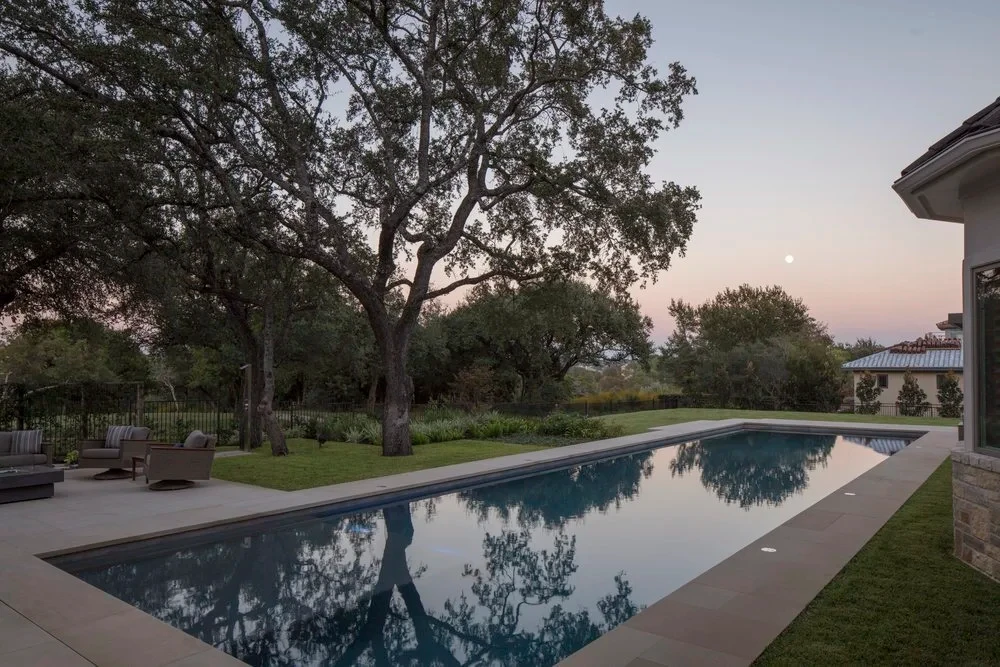 Geometric pool reflecting a rising moon and oaks over a lawn beside a stone home in Barton Creek